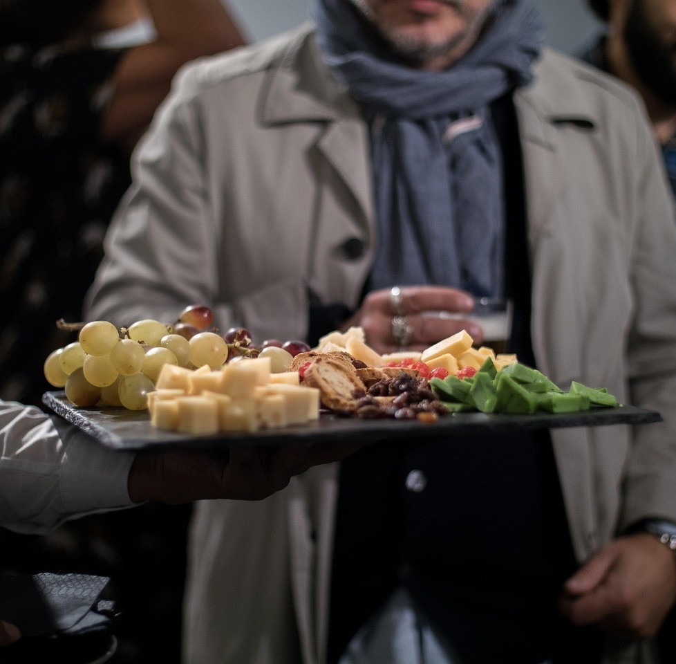 Caterign serveing hold a board covered with food infront of a man.